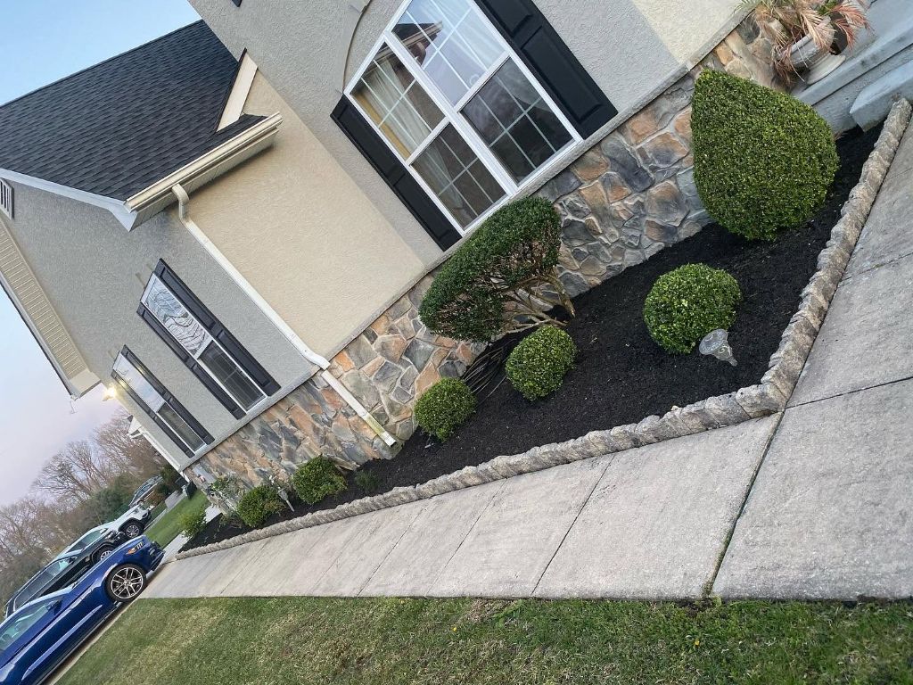 Black mulch planting beds with shrubs and hostas along driveway